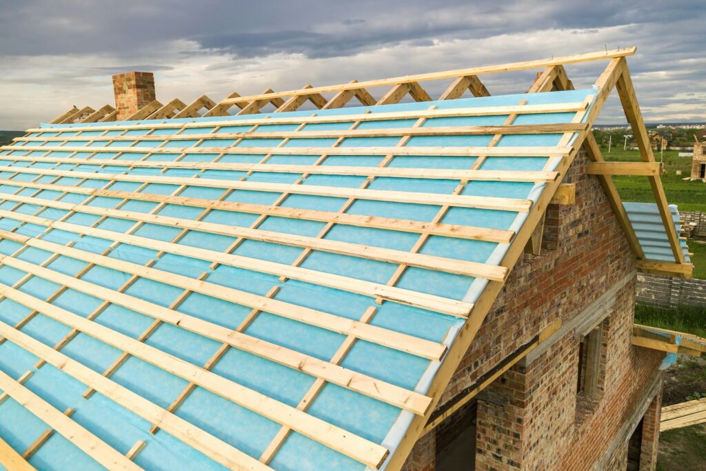 Aerial view of a brick house with wooden roof frame under construction.