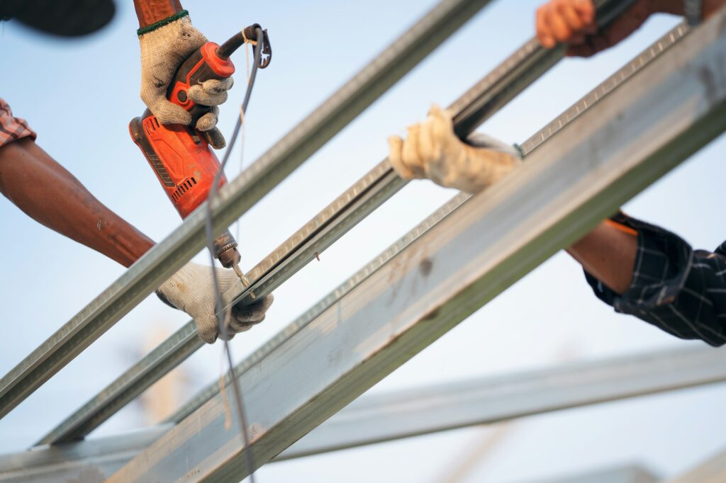 Man worker uses a power drill to attach a cap metal roofing job with screws.